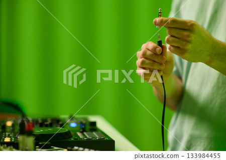 DJ setup closeup, Close view of audio connection process during live performance, Detailed image capturing technician connecting audio cables to mixer with ambient lighting 133984455