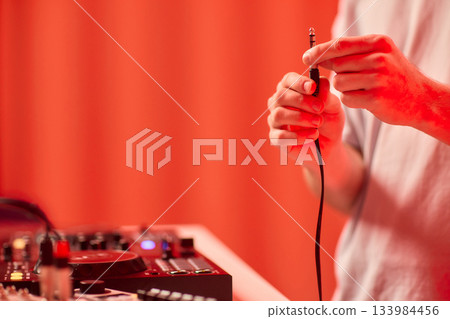 DJ setup closeup, Close view of audio connection process during live performance, Detailed image capturing technician connecting audio cables to mixer with ambient lighting DJ setup closeup, Close view of audio connection process during live performance, Detailed image capturing technician connecting audio cables to mixer with ambient lighting 133984456