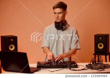 Young DJ with headphones, Skilled DJ engaging with equipment in lively environment, Energetic DJ prepping for live performance amid colorful lighting and fashionable attire Young DJ with headphones, Skilled DJ engaging with equipment in lively environment, Energetic DJ prepping for live performance amid colorful lighting and fashionable attire 133984464