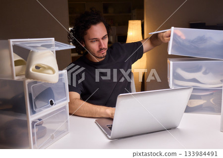 Individual systematically records shoe information on computer in workspace, Person carefully inputs sneaker details into spreadsheet within tidy home office environment 133984491