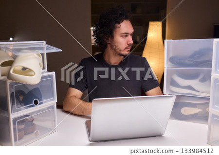 Individual systematically records shoe information on computer in workspace, Person carefully inputs sneaker details into spreadsheet within tidy home office environment Individual systematically records shoe information on computer in workspace, Person carefully inputs sneaker details into spreadsheet within tidy home office environment 133984512