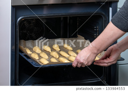 Placing Tray of Unbaked Meat Patties Into Oven on Parchment-Lined Baking Sheet Placing Tray of Unbaked Meat Patties Into Oven on Parchment-Lined Baking Sheet 133984553