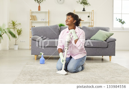 Young cheerful woman housewife in rubber gloves sitting om the floor with vacuum cleaner at home 133984556