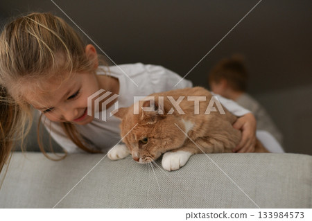 A girl near a ginger cat on the couch 133984573