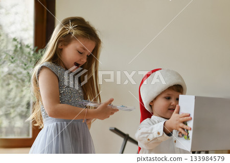 A boy in a santa hat and girl unpacking the christmas presents 133984579