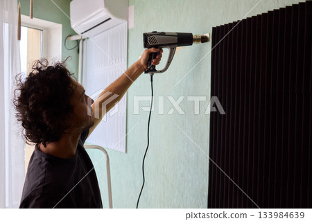 Craftsman carefully detaching acoustic panels indoors, Individual skillfully peels acoustic insulation from wall using heat and precise hand movements for studio setup Craftsman carefully detaching acoustic panels indoors, Individual skillfully peels acoustic insulation from wall using heat and precise hand movements for studio setup 133984639