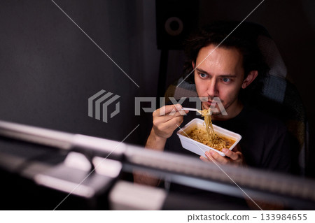Live streaming snack, Content creator enjoys snack during livestream break, Casual moment captured during evening stream with ambient glow and home studio background 133984655