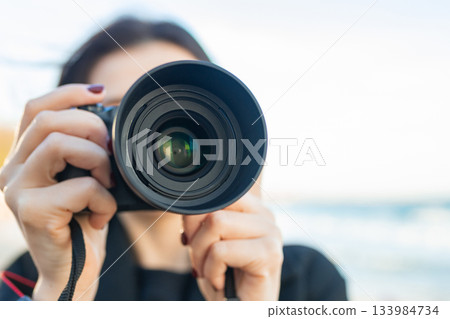 Low-angle view of a female photographer holding a professional camera against the blue sky, capturing outdoor moments and focusing on creative photography. 133984734