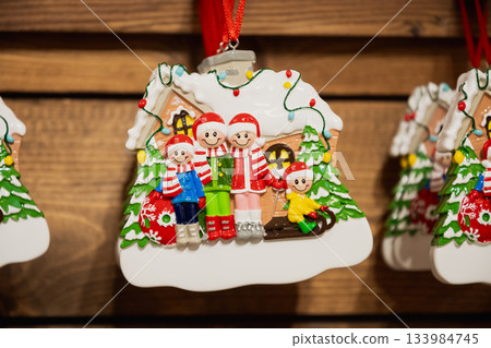Close up of gingerbread style family Christmas ornament hanging on wooden display, colorful holiday decoration at festive market in kiosk. Close up of gingerbread style family Christmas ornament hanging on wooden display, colorful holiday decoration at festive market in kiosk. 133984745