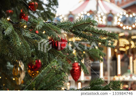 Close up of decorated Christmas tree branch with red ornaments and warm lights at festive holiday market background, cozy winter atmosphere. Close up of decorated Christmas tree branch with red ornaments and warm lights at festive holiday market background, cozy winter atmosphere. 133984746