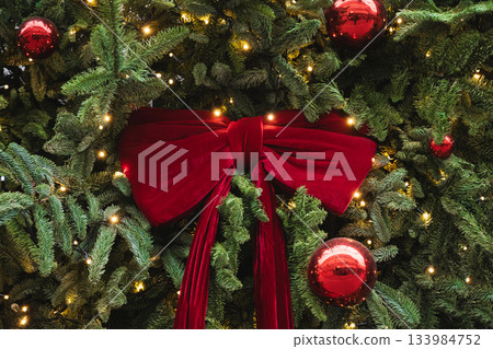 Christmas tree decorated large red velvet bow and glowing lights. Xmas card. Winter holiday spirit. Decorative shop window. Outdoors. Christmas tree decorated large red velvet bow and glowing lights. Xmas card. Winter holiday spirit. Decorative shop window. Outdoors. 133984752