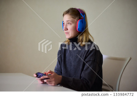 Casual female gamer with cerebral palsy, Relaxed woman with gaming controller, Young woman plays video game comfortably at home, Female gamer intently engaging with console in cozy living space 133984772