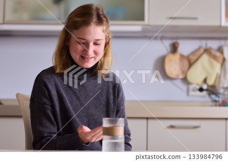 Self reliant woman handles morning pills in peaceful kitchen setting, Woman with cerebral palsy diligently manages her daily medication routine independently at home 133984796