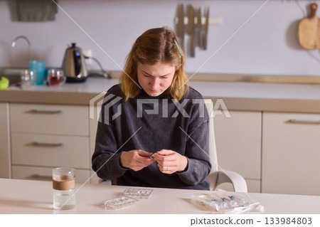 Self reliant woman handles morning pills in peaceful kitchen setting, Woman with cerebral palsy diligently manages her daily medication routine independently at home 133984803