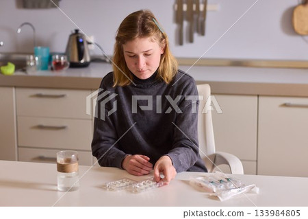 Self reliant woman handles morning pills in peaceful kitchen setting, Woman with cerebral palsy diligently manages her daily medication routine independently at home 133984805