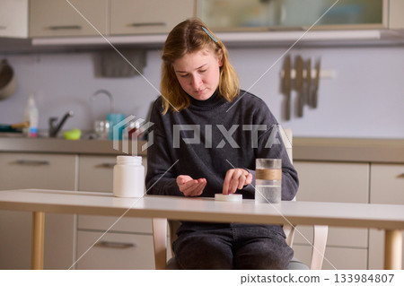 Self reliant woman handles morning pills in peaceful kitchen setting, Woman with cerebral palsy diligently manages her daily medication routine independently at home 133984807
