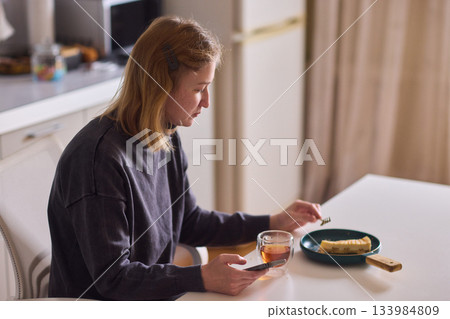 cerebral palsy Young woman smiling with tea and cheesecake, Casual domestic setting featuring woman indulging and relaxing, Relaxed young woman savoring cake and tea at sunlit kitchen table 133984809