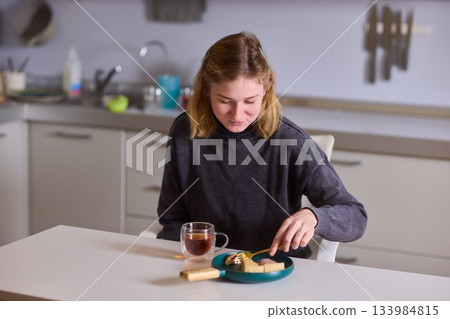 cerebral palsy Young woman smiling with tea and cheesecake, Casual domestic setting featuring woman indulging and relaxing, Relaxed young woman savoring cake and tea at sunlit kitchen table 133984815