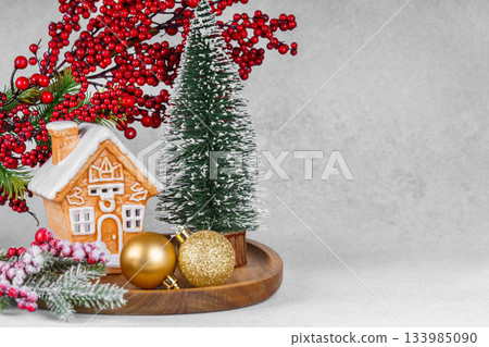 Gingerbread style ceramic Christmas house with ornaments, holly berries and snowy spruce tree 133985090