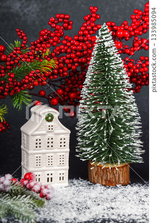 Ceramic Christmas house with pine Tree and winter decorations on black background with snow Ceramic Christmas house with pine Tree and winter decorations on black background with snow 133985094