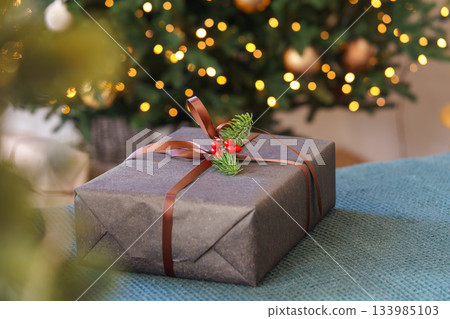 Christmas gift box decorated with ribbon and red berries in front of glowing festive tree lights 133985103