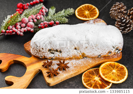 Traditional Christmas Stollen, sweet fruit loaf with sugar icing on wooden board and festive decor 133985115