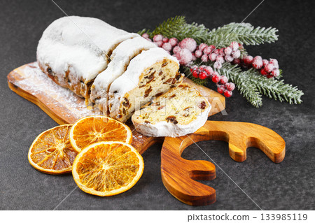 Traditional sliced Christmas stollen loaf with raisins and powdered sugar on wooden cutting board 133985119