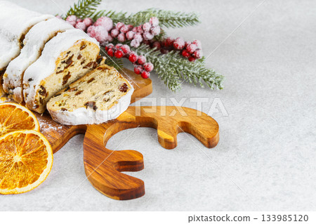 Traditional sliced Christmas stollen loaf with raisins and powdered sugar on wooden cutting board 133985120