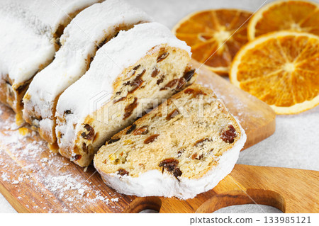 Traditional sliced Christmas stollen loaf with raisins and powdered sugar on wooden cutting board Traditional sliced Christmas stollen loaf with raisins and powdered sugar on wooden cutting board 133985121