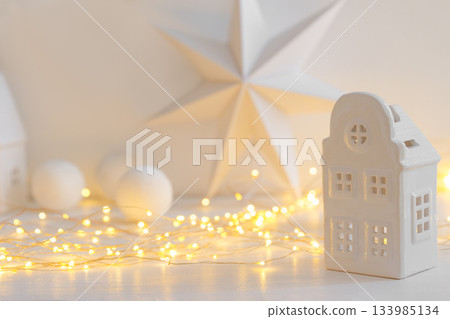 Minimalist Christmas decor, ceramic house on garland warm festive fairy lights background 133985134