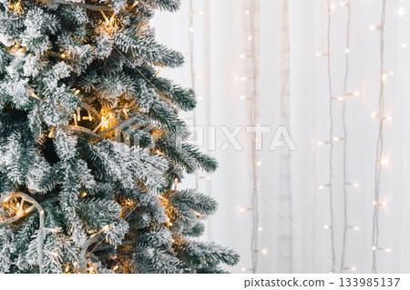 Snowy frosted Christmas tree branches with ornaments on warm string lights illumination background Snowy frosted Christmas tree branches with ornaments on warm string lights illumination background 133985137