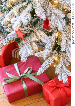 Red wrapped gift boxes, presents under festive Christmas tree with lights and holiday decorations Red wrapped gift boxes, presents under festive Christmas tree with lights and holiday decorations 133985138
