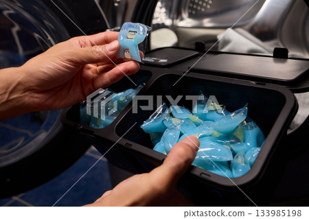 Laundry pod placement, Load blue detergent capsules into machine for hygienic washing, Preparing laundry by placing capsules carefully into washing machine for cleanliness 133985198
