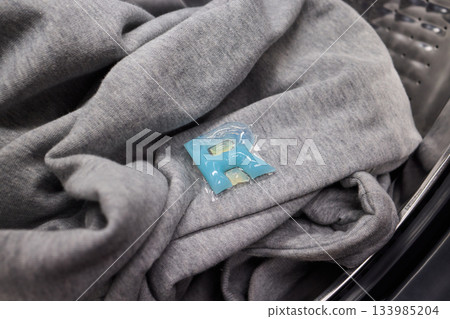 Inspecting laundry pod on sweater, Closeup of hands testing cleaning tablet, Detailed view of hand assessing laundry pod for quality and proper dissolution process Inspecting laundry pod on sweater, Closeup of hands testing cleaning tablet, Detailed view of hand assessing laundry pod for quality and proper dissolution process 133985204