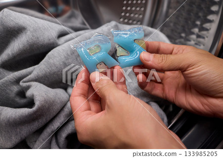 Inspecting laundry pod on sweater, Closeup of hands testing cleaning tablet, Detailed view of hand assessing laundry pod for quality and proper dissolution process 133985205