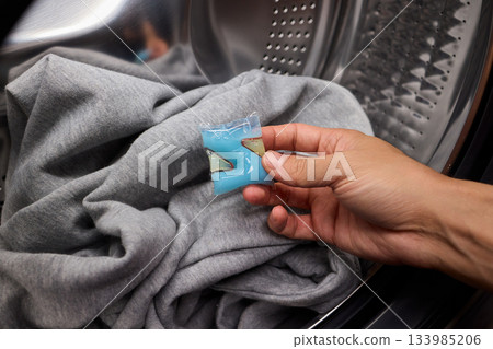 Inspecting laundry pod on sweater, Closeup of hands testing cleaning tablet, Detailed view of hand assessing laundry pod for quality and proper dissolution process 133985206