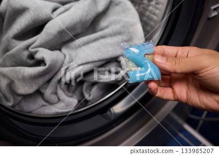 Inspecting laundry pod on sweater, Closeup of hands testing cleaning tablet, Detailed view of hand assessing laundry pod for quality and proper dissolution process 133985207