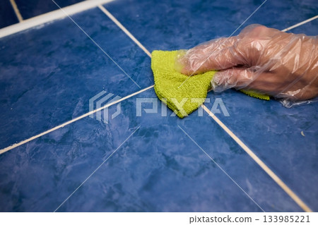 Hand cleaning grout, Scrubbing ceramic tile joints professionally, Detailed hand scrub of grout with sponge and gloves, Closeup of hand using sponge to clean grout lines Hand cleaning grout, Scrubbing ceramic tile joints professionally, Detailed hand scrub of grout with sponge and gloves, Closeup of hand using sponge to clean grout lines 133985221