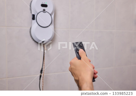 Smart robot performing quick hygienic maintenance in bathroom space, Modern robotic cleaner diligently scrubbing grout lines adjacent to toilet in bright tiled room 133985223