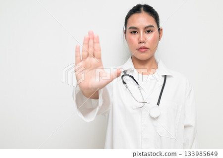 Woman Doctor with Stethoscope in White Uniform on Plain Background Doing Stop Rejection Gesture Woman Doctor with Stethoscope in White Uniform on Plain Background Doing Stop Rejection Gesture 133985649