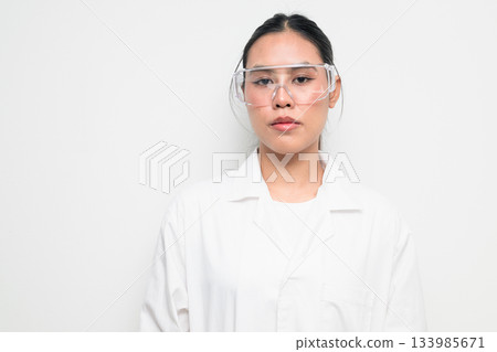 Female Scientist in Protective Goggles and Lab Coat on White Background Female Scientist in Protective Goggles and Lab Coat on White Background 133985671
