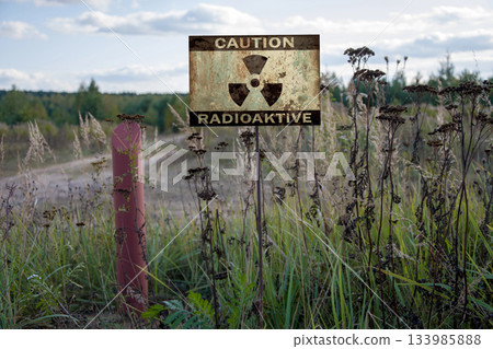 Rusty sign with the inscription: caution, radiation, exclusion zone, contaminated area, withered plants. 133985888