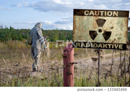 Military dosimetrist measures the radiation area, a sign with the inscription: caution, radiation, chemical protective suit and gas mask Military dosimetrist measures the radiation area, a sign with the inscription: caution, radiation, chemical protective suit and gas mask 133985890