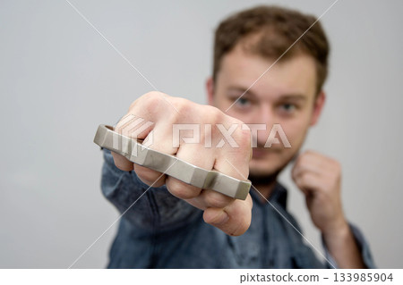 Man strikes brass knuckles on a light background, a prohibited weapon in a fight, heavy damage 133985904