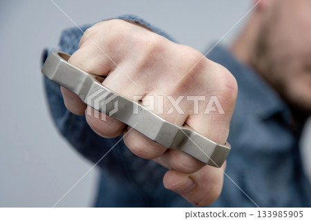 Man strikes brass knuckles on a light background, a prohibited weapon in a fight Man strikes brass knuckles on a light background, a prohibited weapon in a fight 133985905