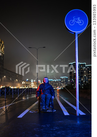 Motivated man with disability in wheelchair in rgb neon light on night walk outdoors to keep active. 133985993
