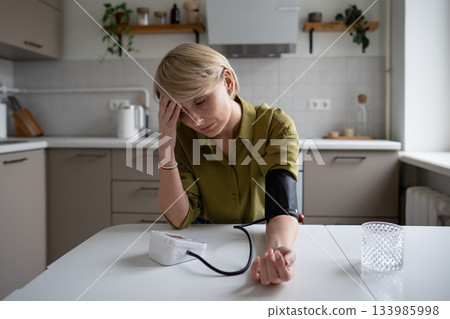 Middle aged woman with low blood pressure and lack of energy measuring blood pressure with tonometer 133985998