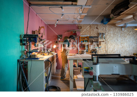 Man carpenter works on order in carpentry workshop, manufacturing unique wooden furniture items. 133986025