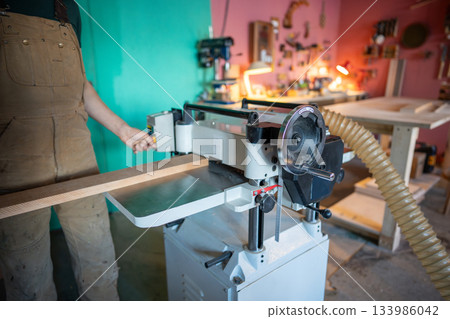 Skilled craftsman working with wood on planer thicknesser jointer, preparing furniture materials 133986042