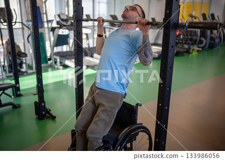 Motivated man in wheelchair do vertical pull to strengthen arms and back. Inclusive adaptation Motivated man in wheelchair do vertical pull to strengthen arms and back. Inclusive adaptation 133986056